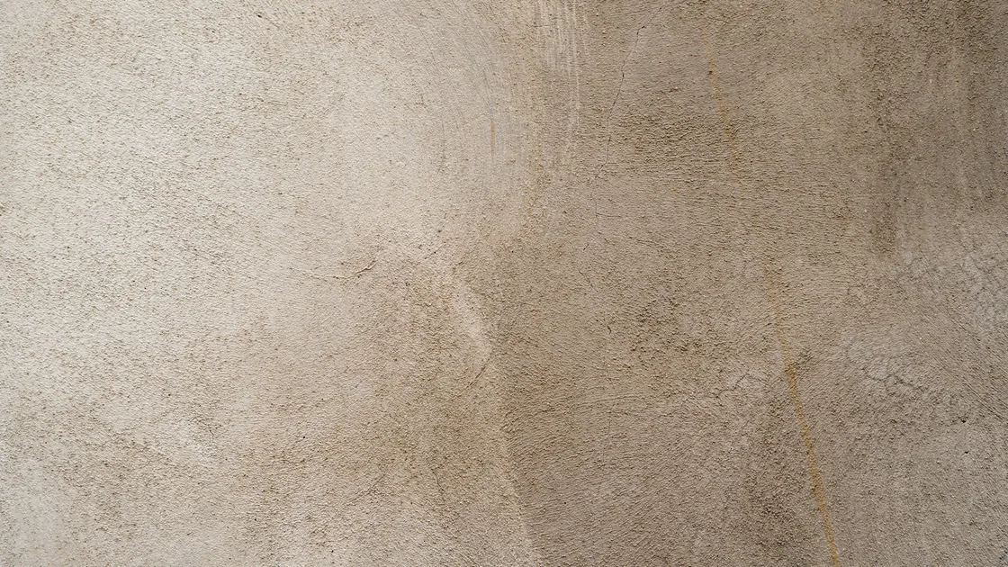 Superficie de un muro revestido con mortero de cal, con textura irregular y tonos beige y arena